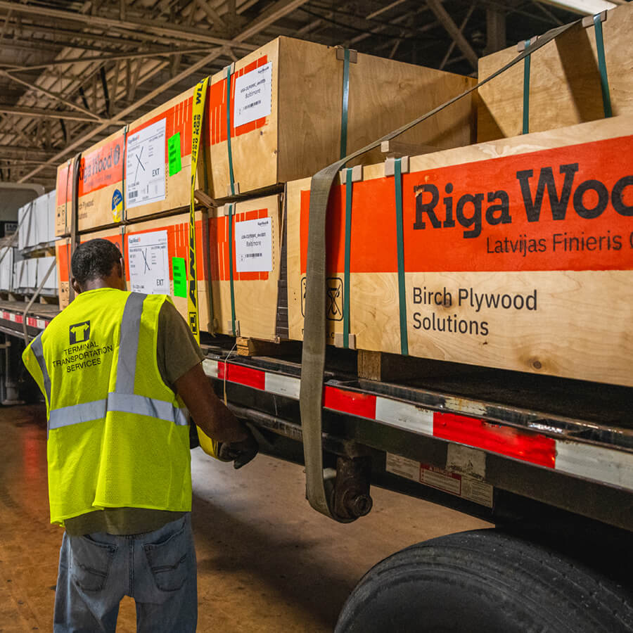 employee strapping load of palletized plywood to flatbed trailer